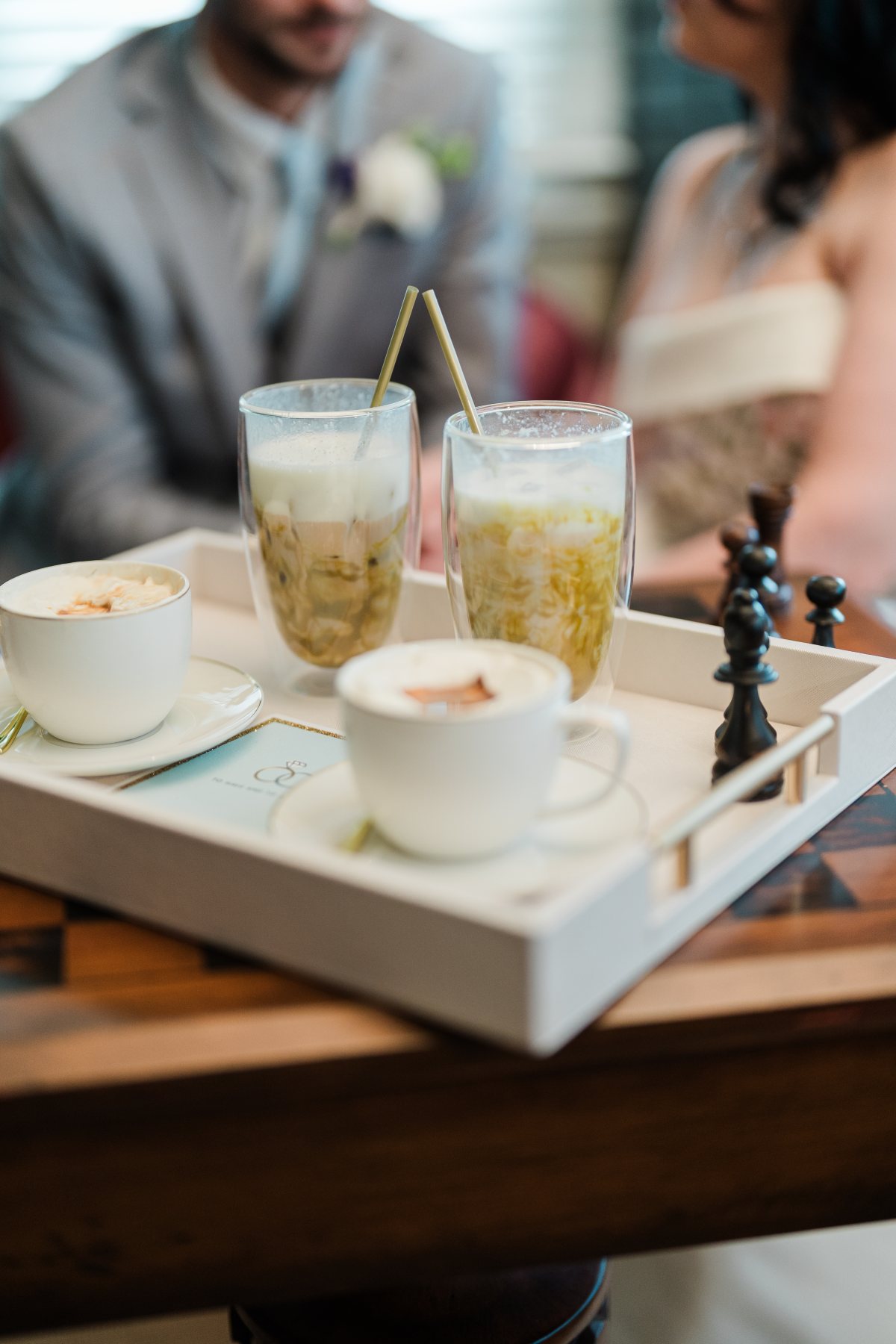 Iced coffees in tall glasses and china cups served on a tray at the couple’s table