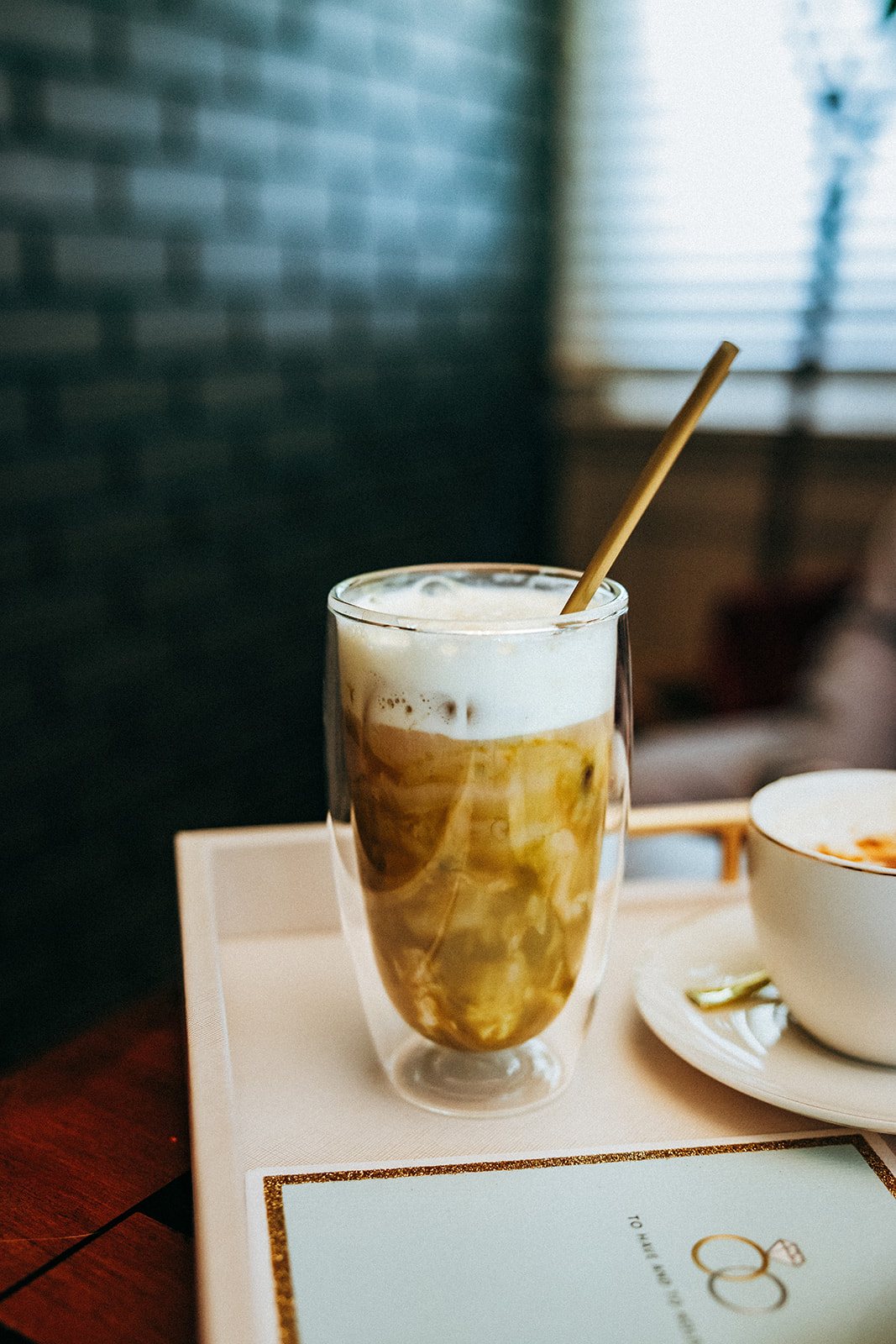 An iced latte with a gold straw served on a tray beside a personalized card