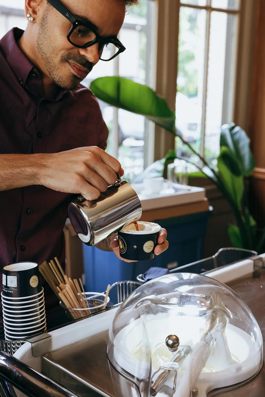 Sam pouring a Love Affogato at the cart, sunlit lounge behind