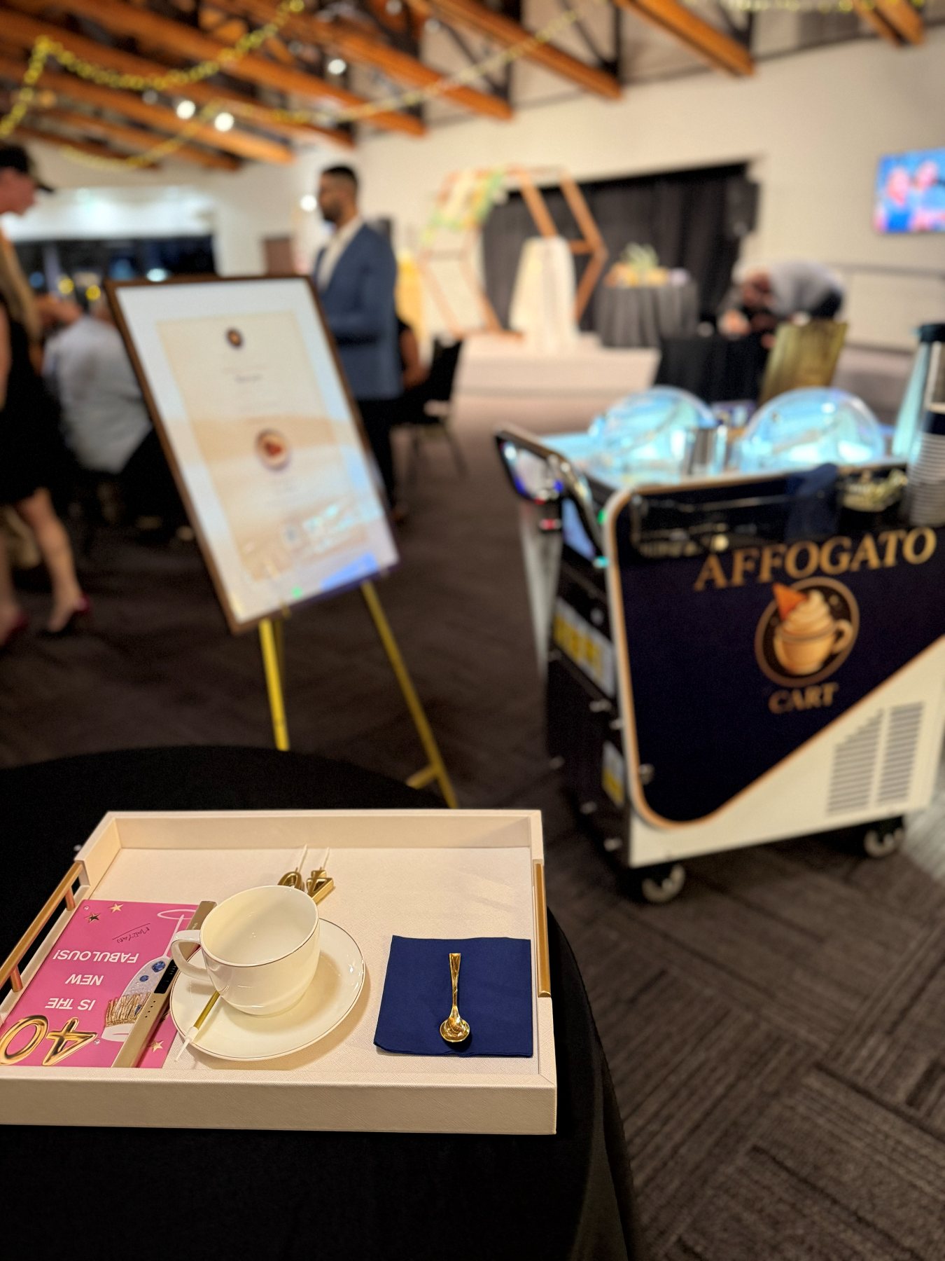 The special serving tray with a china cup and gold spoon at a 40th birthday celebration, with the menu easel and the cart behind